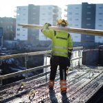 Karriere: Mann med Betonmast arbeidsklær bærer på planker på et høyt bygg